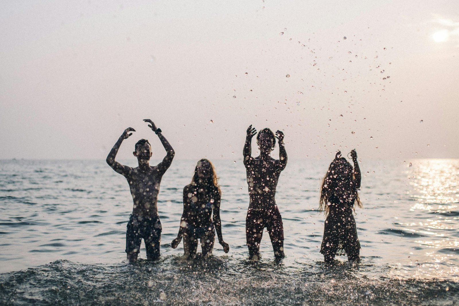 Group of friends having fun in the ocean, silhouetted against a sunset sky.
